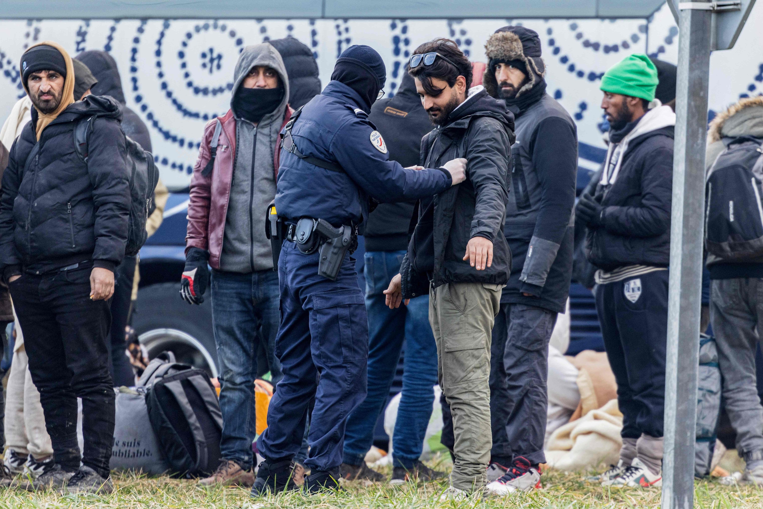 Een Franse politieagent fouilleert een migrant in Loon-Plage, nabij Duinkerke.