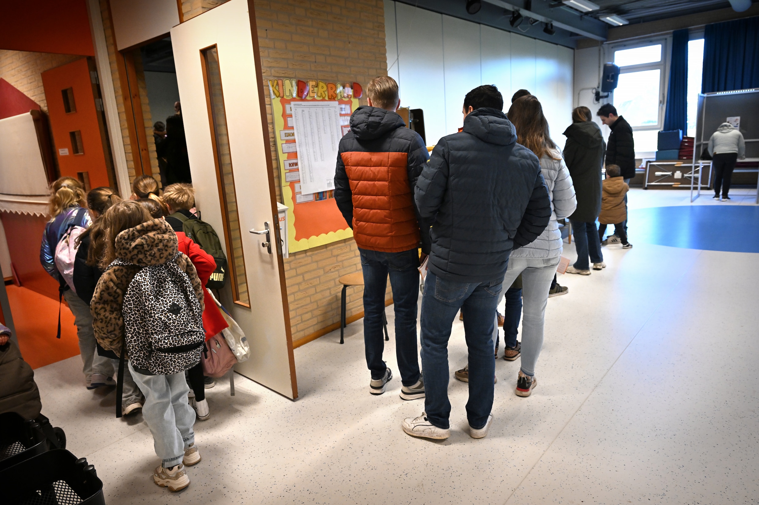 Terwijl de kinderen in de rij staan voorhun les begint, wachten hun ouders in de rij voor het stembureau.