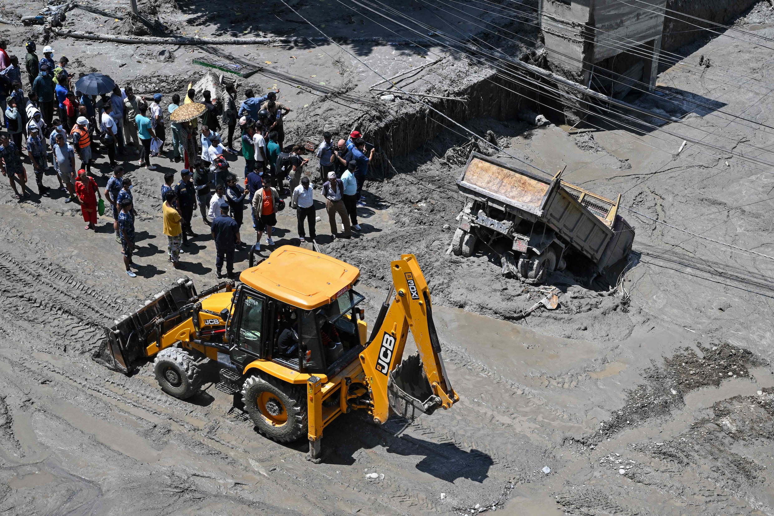 Mensen kijken toe terwijl een bulldozer modder en puin van de weg ruimt na de overstromingen in Trishuli.