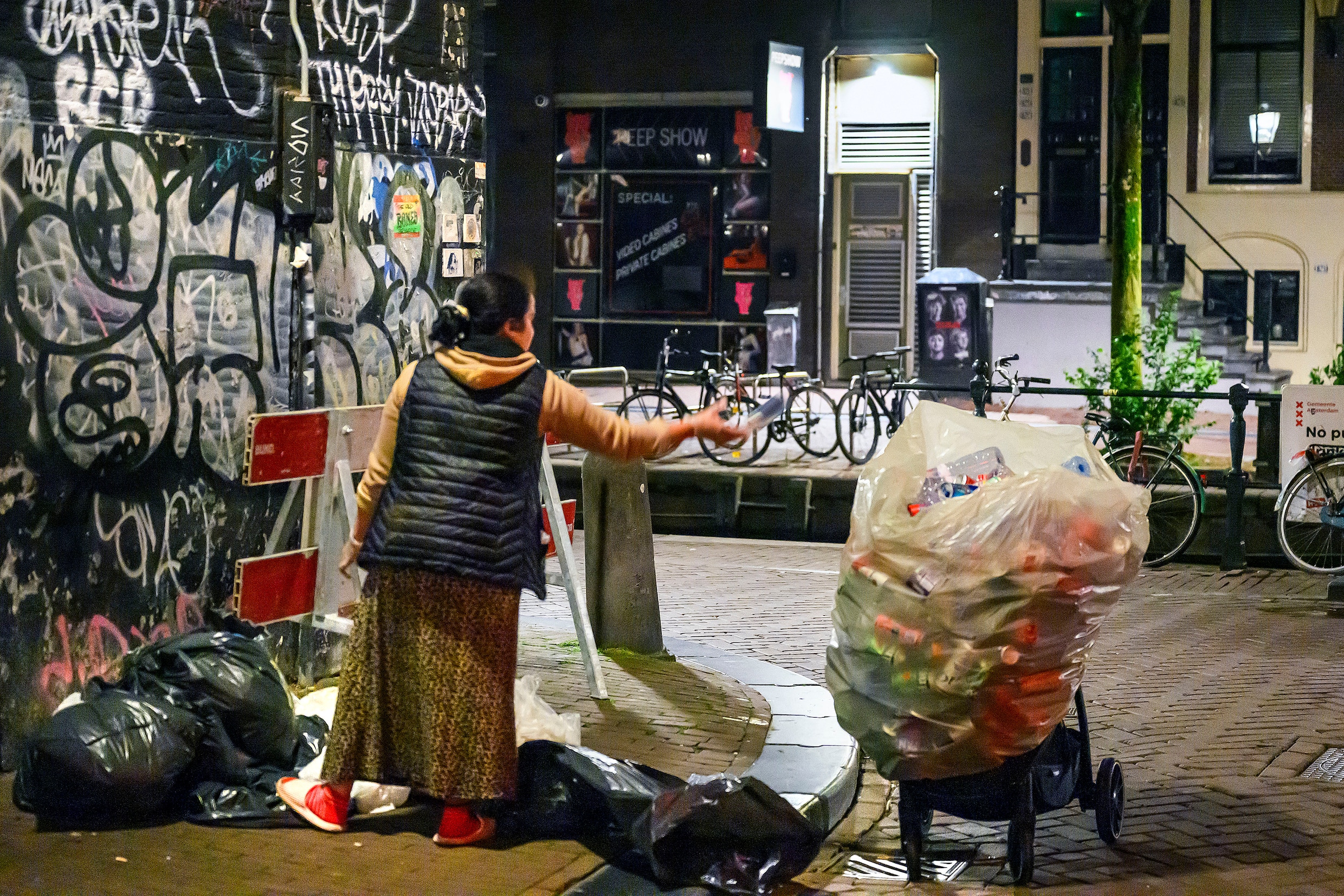 Op de Wallen in Amsterdam verzamelt een vrouw statiegeldblikjes en -flessen die ze onder meer vindt in vuilniszakken op straat.