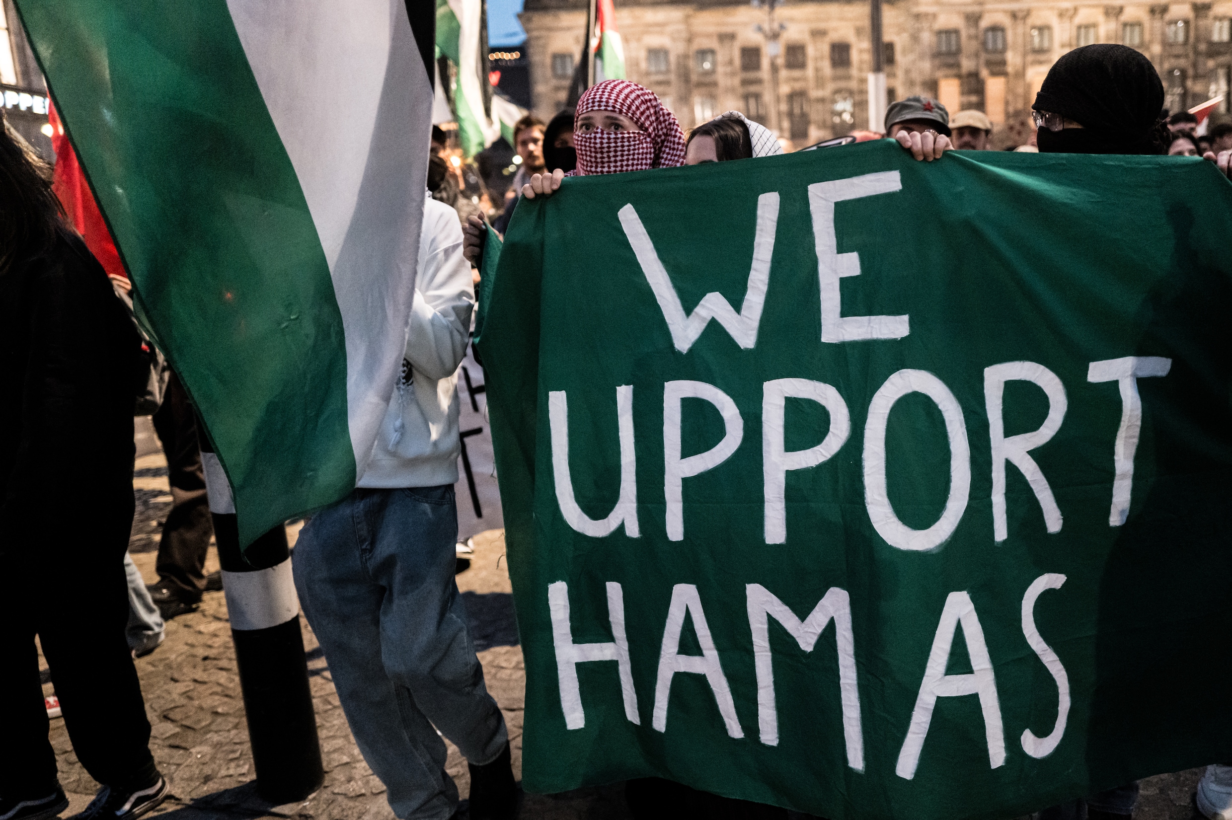  Gemaskerde demonstranten houden op de Dam een groen spandoek met de tekst ‘We support Hamas’ omhoog.